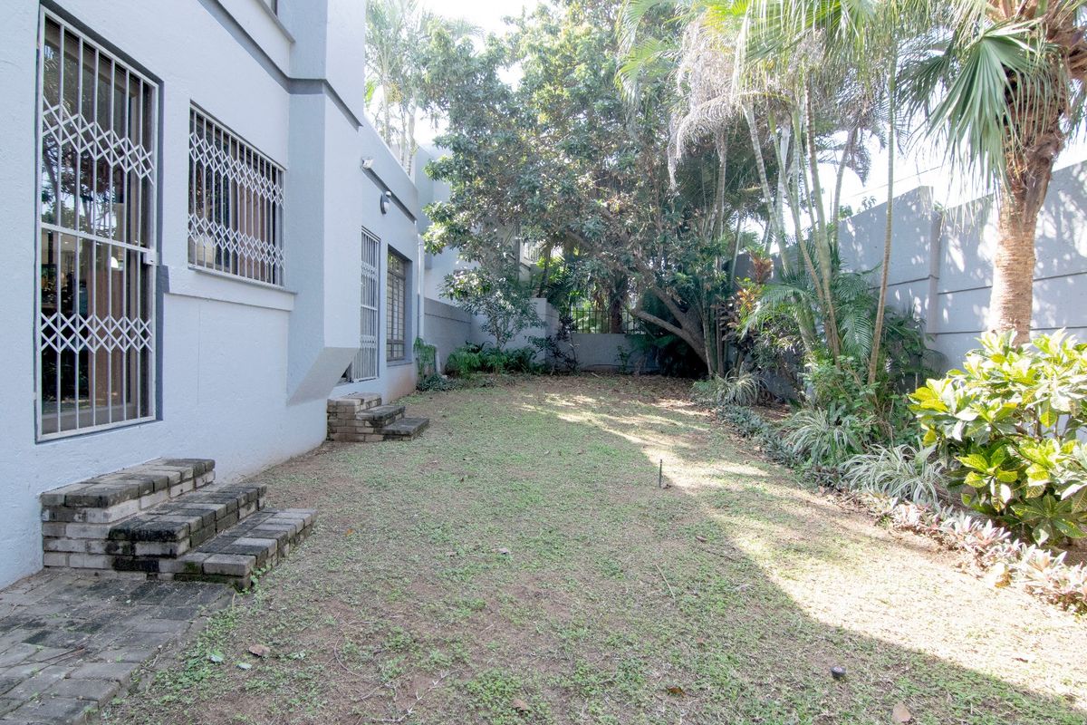 A private rear garden featuring a lawn area, mature trees, perimeter boundary walls, and direct access to the house via brick steps.