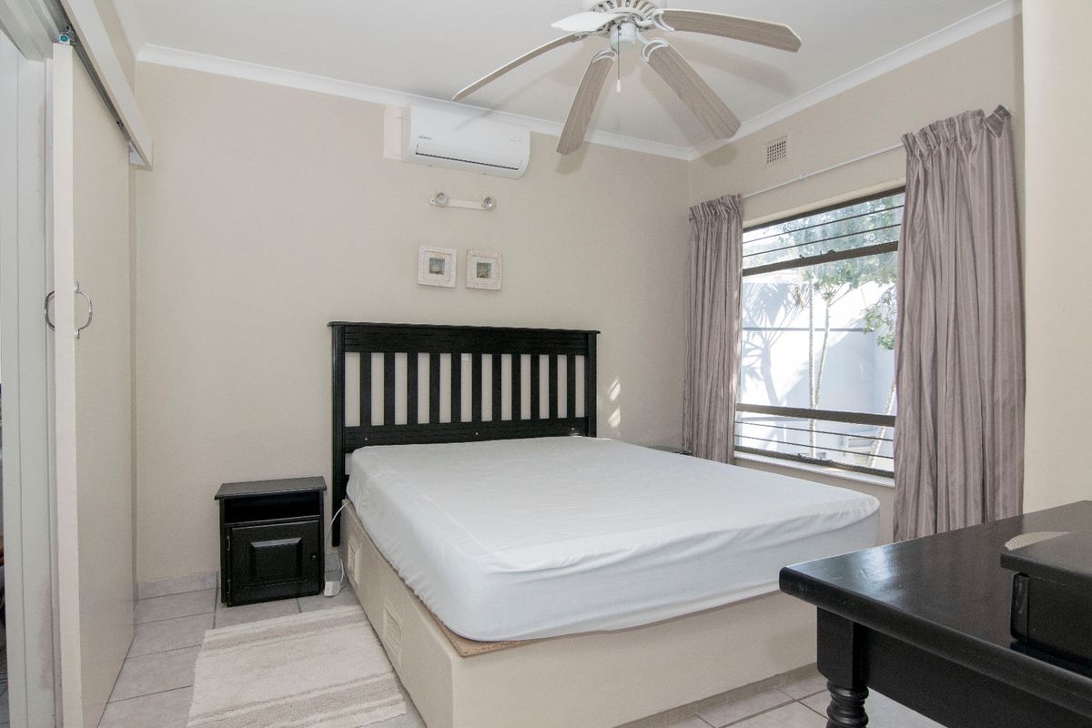 A bedroom featuring tiled flooring, a ceiling fan, and a wall-mounted air conditioning unit, with built-in sliding door cupboards.