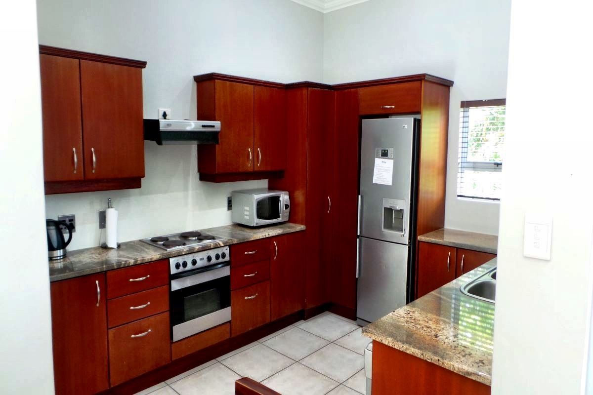 A functional kitchen featuring dark wood cabinetry, granite countertops, a built-in oven, hob, extractor fan, and tiled flooring.