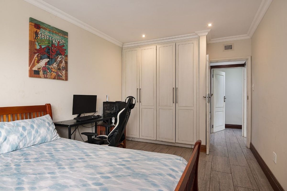 A well-maintained bedroom featuring built-in cupboards, tiled flooring, crown molding, and recessed downlighting, providing a clean and functional living space.