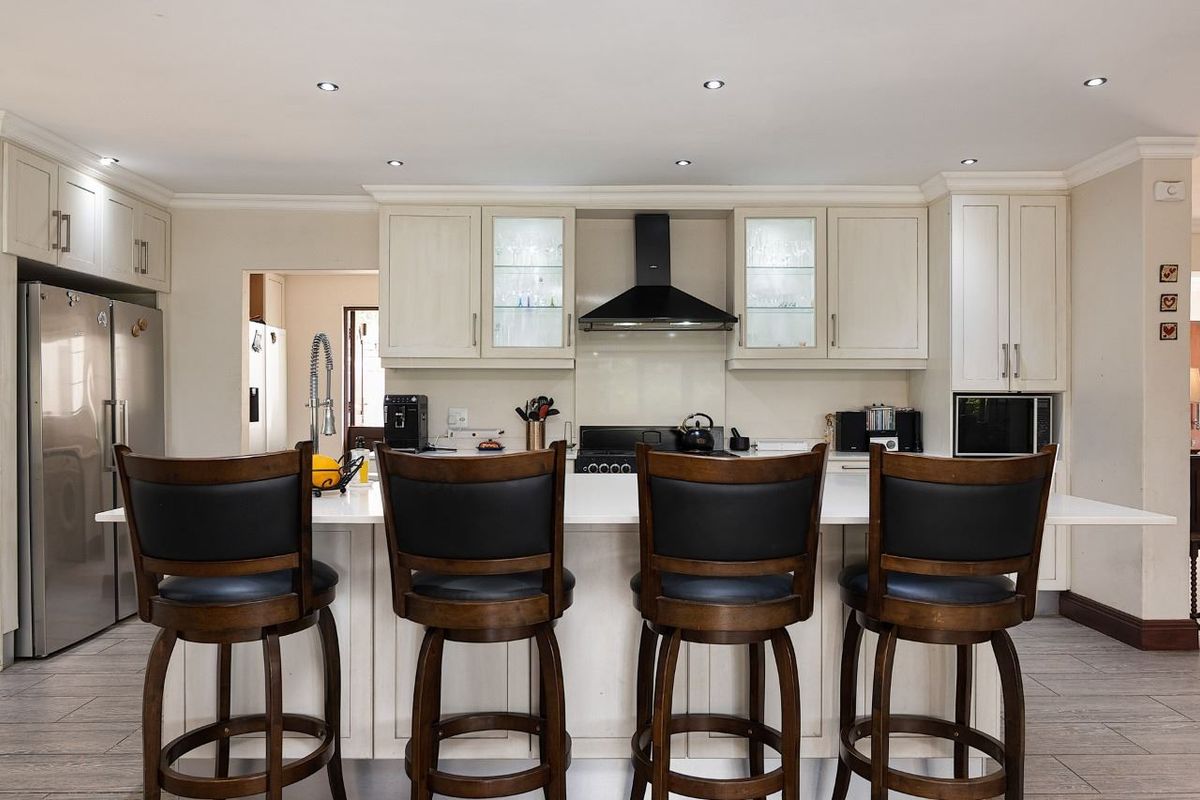 A well-appointed kitchen featuring cream cabinetry, stone countertops, a central island with breakfast bar seating, and modern integrated appliances.