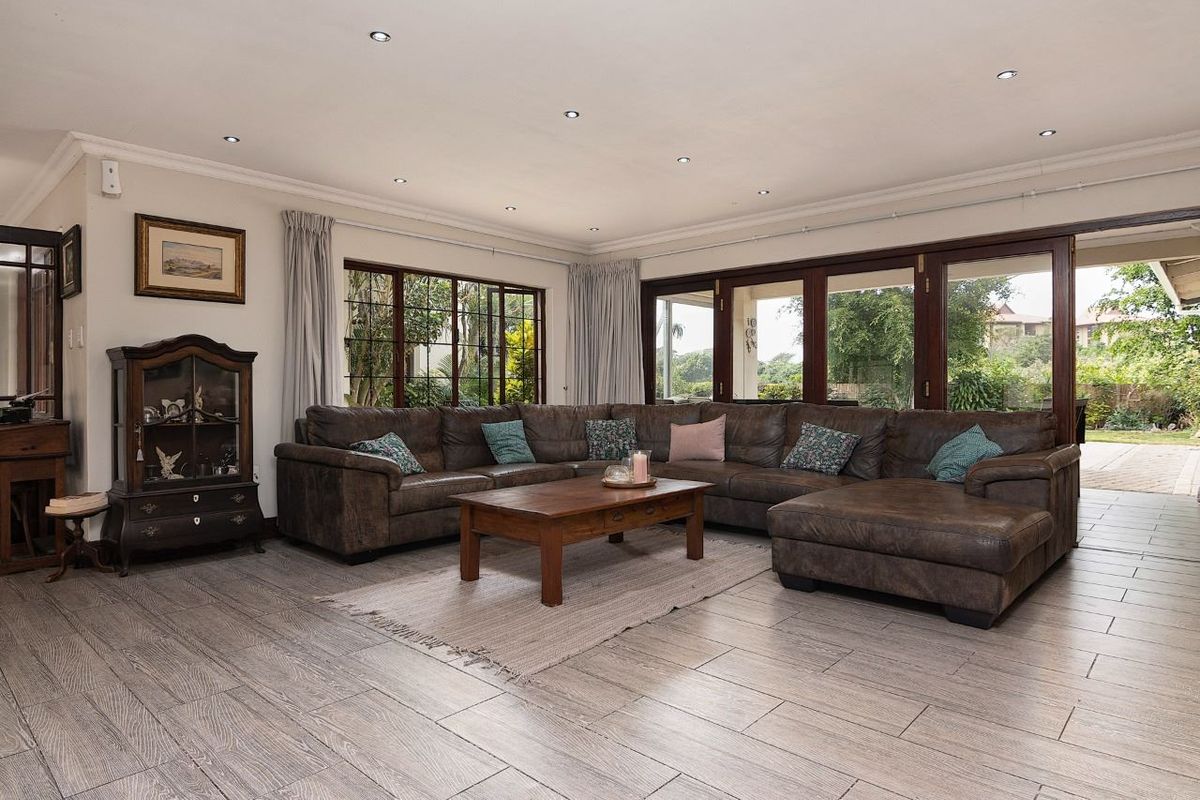 Spacious living room featuring timber-look floor tiles, recessed downlights, and large timber-framed folding doors providing seamless access to the outdoor patio area.