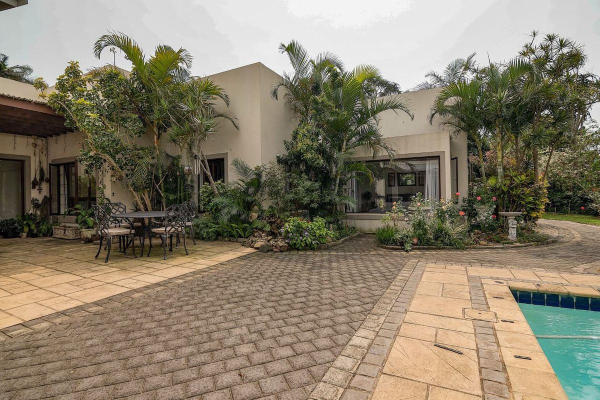 A well-maintained rear exterior featuring a paved patio area, swimming pool, and established garden landscaping adjacent to the main dwelling.