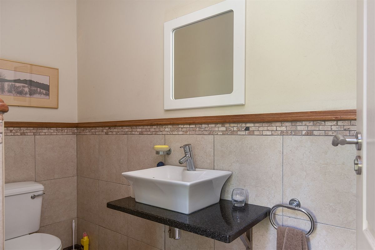 A compact guest bathroom featuring a modern vessel sink on a granite vanity top, tiled walls with a decorative border, and a wall-mounted mirror.