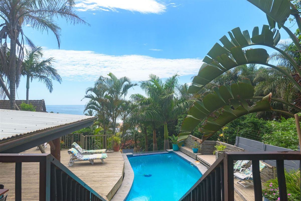 Outdoor pool area featuring a timber deck, lush tropical landscaping, and scenic ocean views.