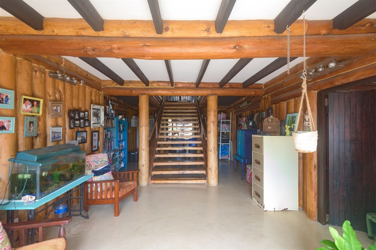 Rustic living area featuring exposed log walls, timber ceiling beams, and a central wooden staircase leading to the upper level.