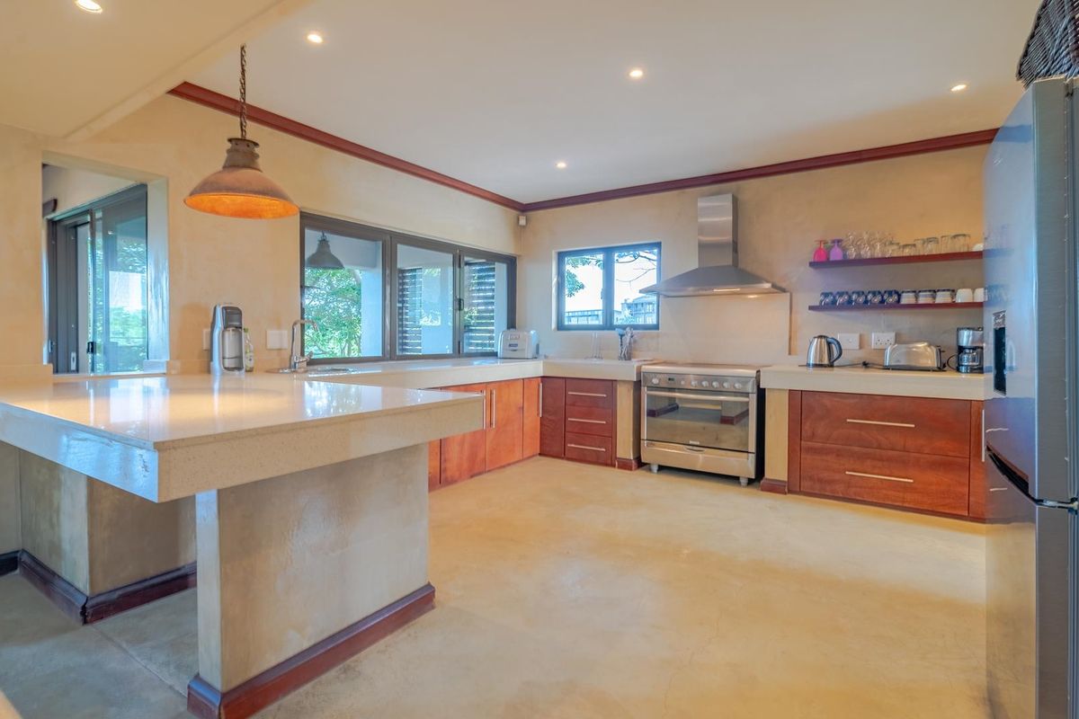 Spacious kitchen featuring stone countertops, warm wood cabinetry, stainless steel appliances, and polished concrete floors with ample natural light.