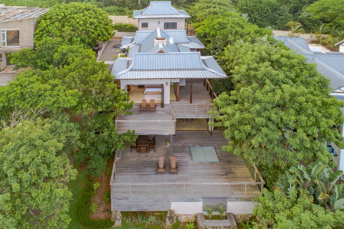 Aerial view of a multi-level residential property featuring extensive timber decking, metal roofing, and lush surrounding greenery.
