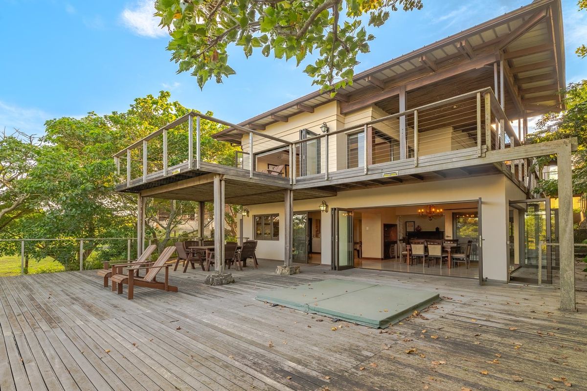 Rear view of a multi-level home featuring a large timber deck, covered patio area, and upper-level balcony with bi-fold doors connecting indoor and outdoor spaces.