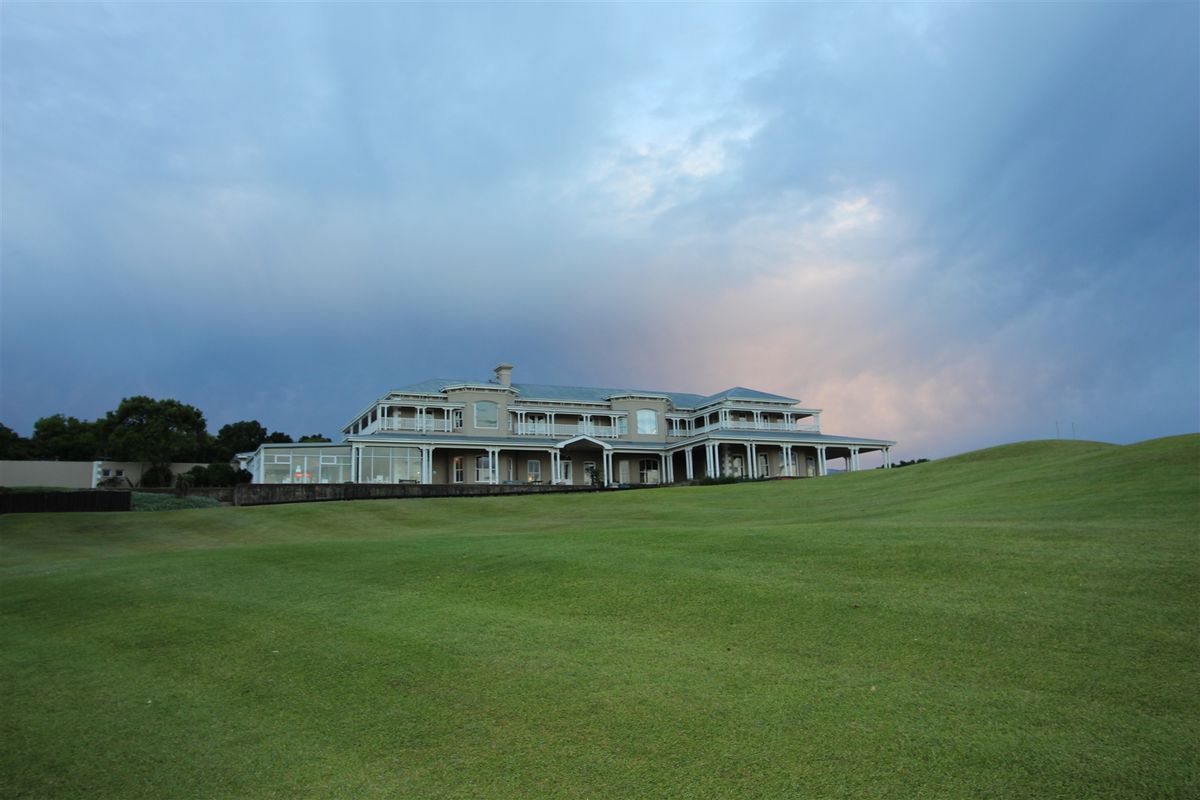 A wide-angle view of the rear elevation of a large residential property, featuring extensive wrap-around balconies and a well-maintained expansive lawn.