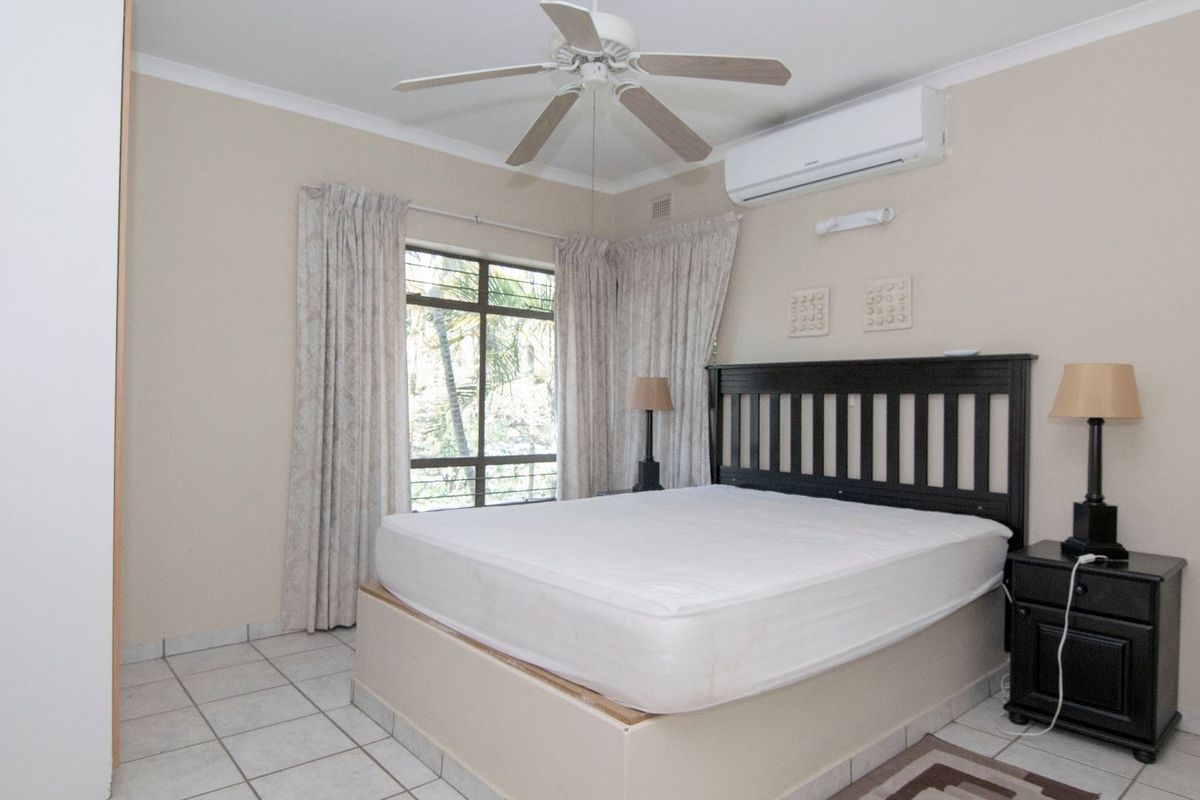 A well-lit bedroom featuring tiled flooring, a ceiling fan, and a wall-mounted air conditioning unit.