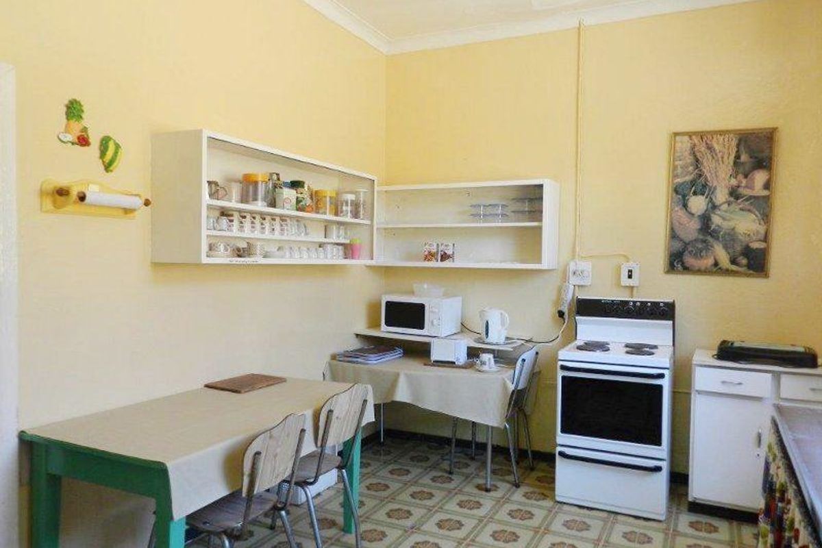 A dated kitchen featuring basic cabinetry, a freestanding stove, and tiled flooring, offering potential for modernization and renovation.
