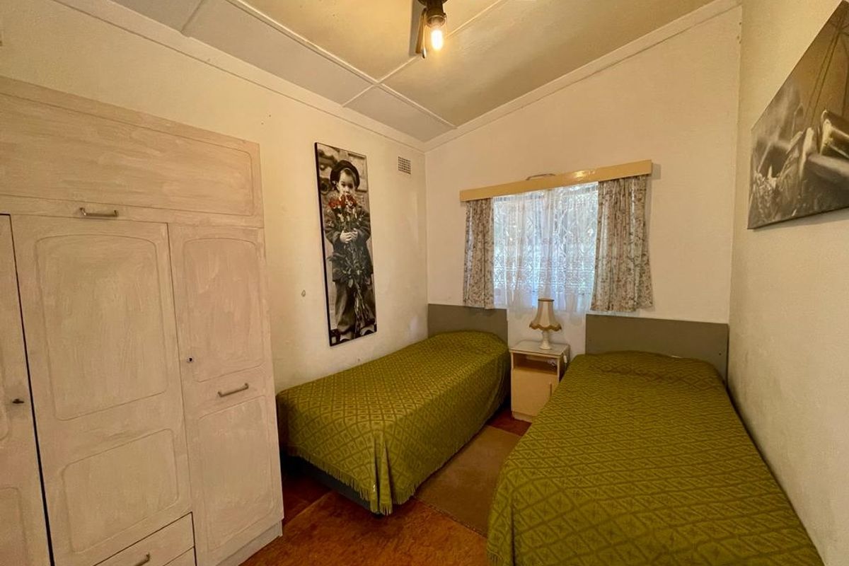 A compact bedroom featuring built-in cabinetry, a ceiling fan, and original flooring, offering a functional space in need of cosmetic updates.