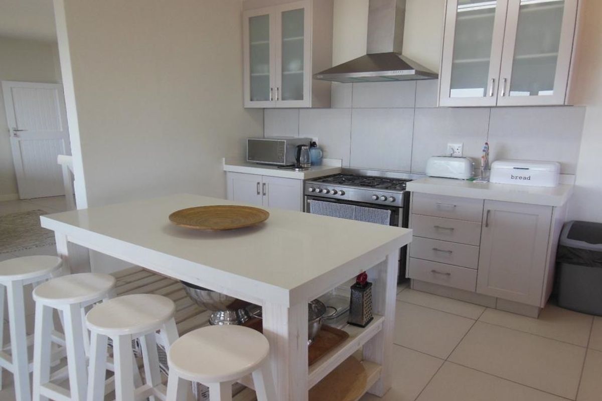A functional kitchen featuring light-toned cabinetry, a stainless steel gas stove with extractor fan, tiled splashbacks, and a central island workspace.