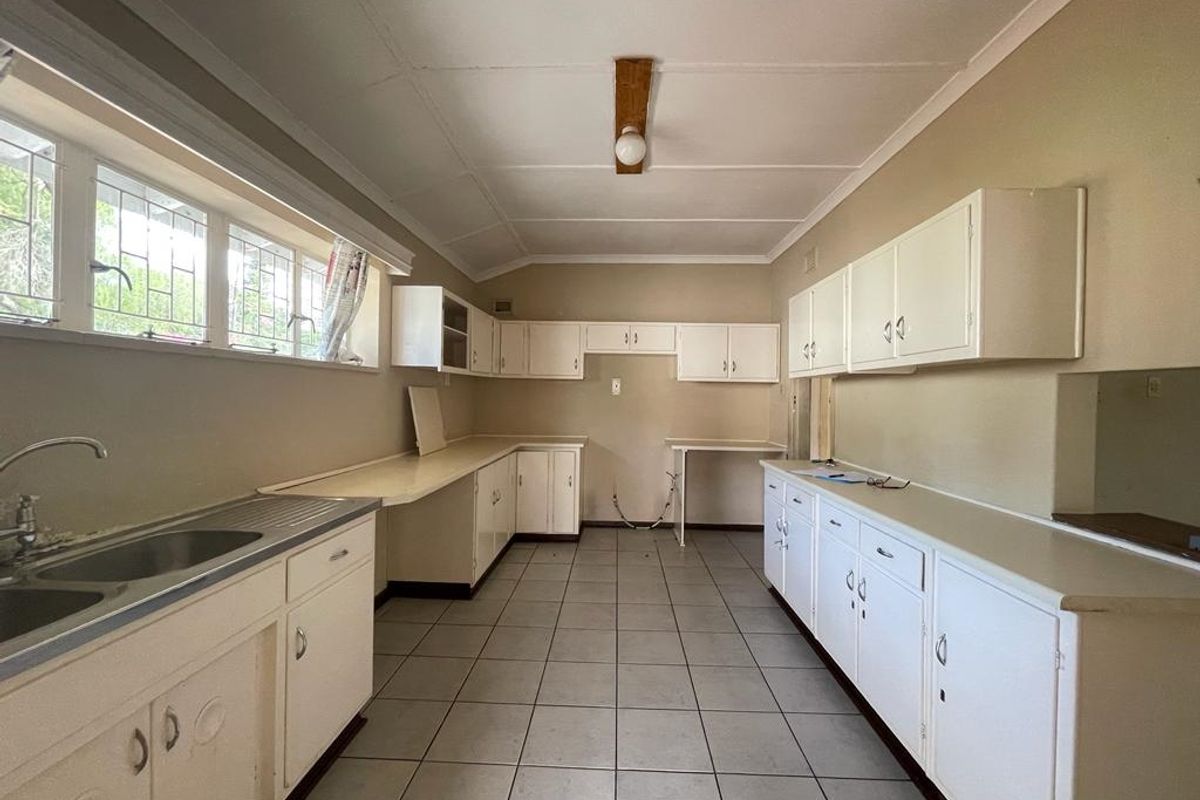 A spacious, dated kitchen featuring extensive white cabinetry, tiled flooring, and ample counter space, offering a blank canvas for modern renovation.