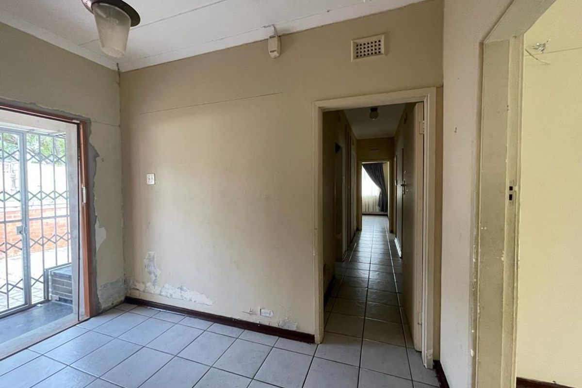 An interior view of a living area featuring tiled flooring, a doorway leading to a hallway, and visible wall surface damage requiring maintenance.