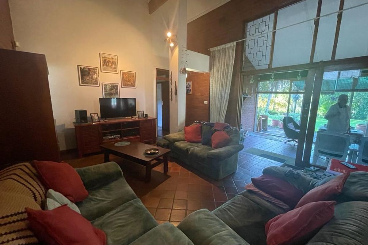 Spacious living room featuring high vaulted ceilings, exposed timber beams, terracotta floor tiles, and large glass sliding doors opening to an outdoor patio area.