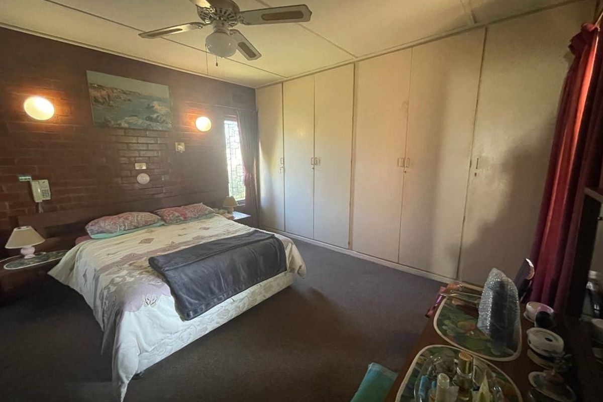Spacious bedroom featuring a brick feature wall, built-in floor-to-ceiling wardrobes, and a ceiling fan.