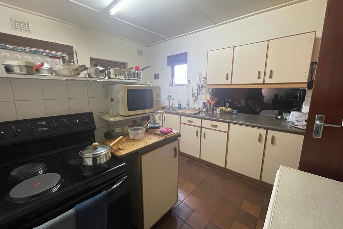 A functional kitchen featuring original cabinetry, tiled flooring, and a freestanding electric stove, offering potential for a modern renovation.