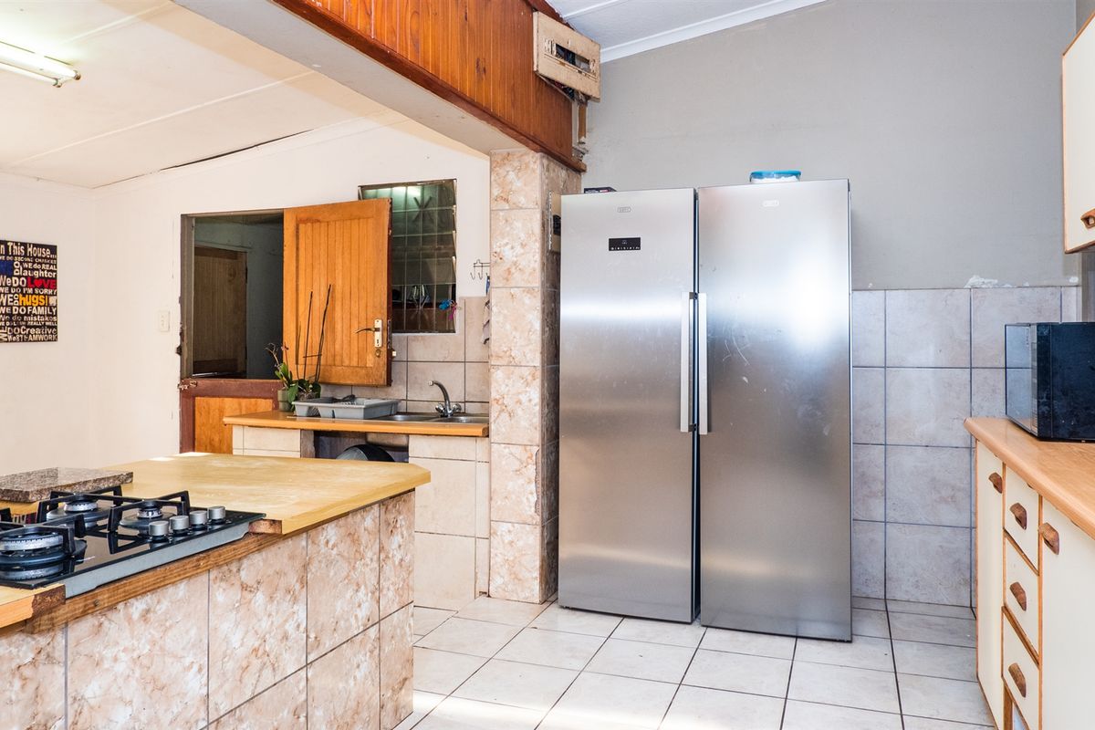 A functional kitchen featuring a central island with a built-in gas hob, tiled countertops, and ample cabinetry, offering a practical layout for daily cooking.