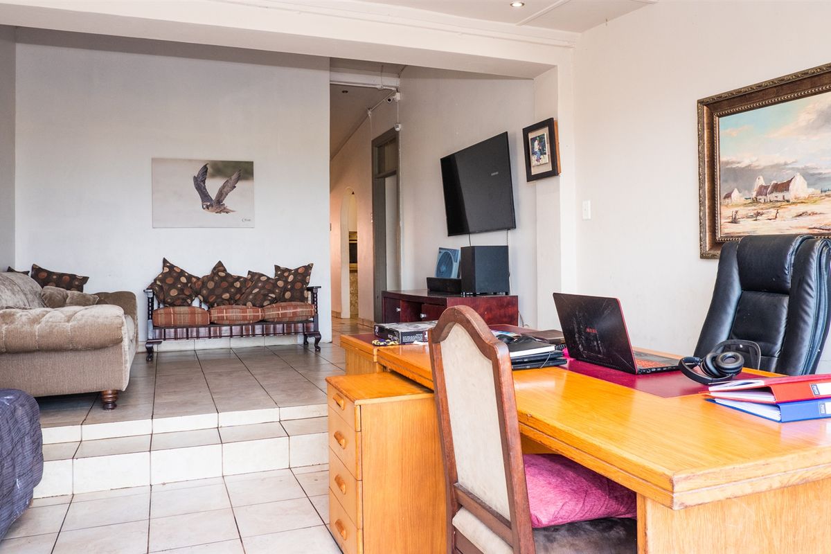 A multi-purpose living and office space featuring tiled flooring, a raised seating area, and direct access to the hallway.