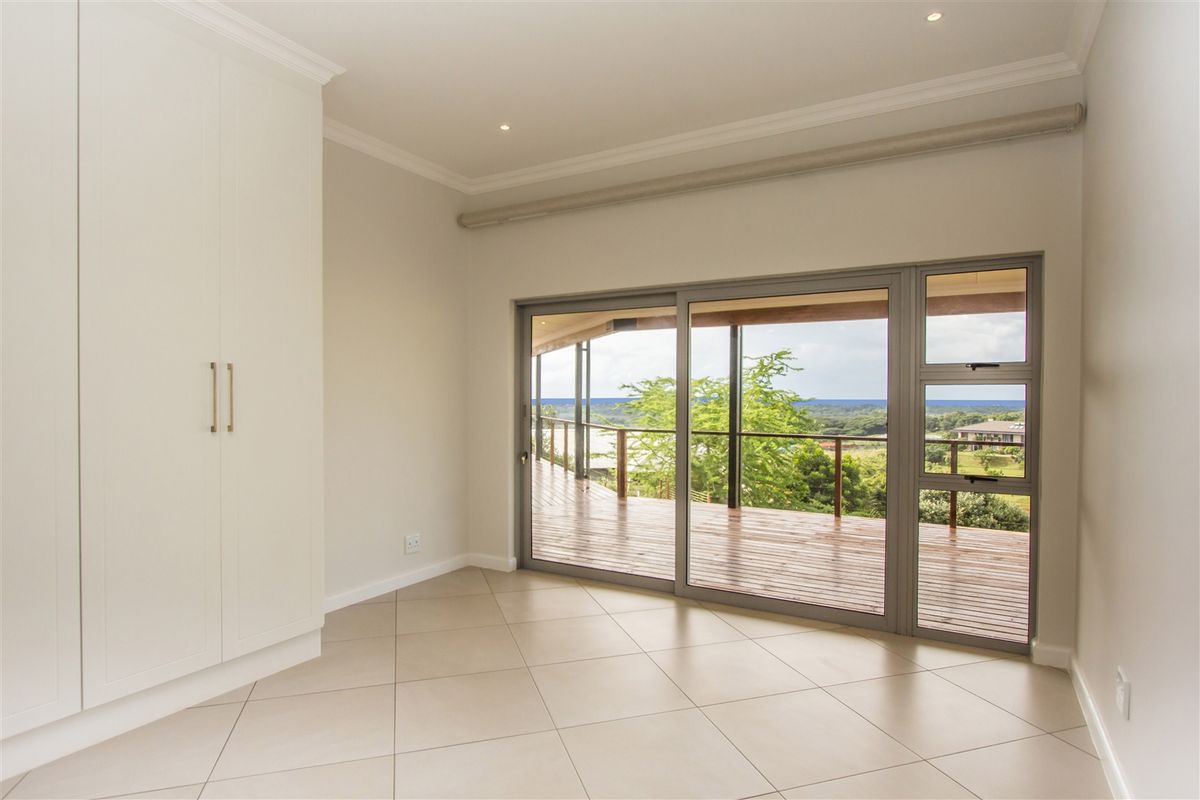 A bright, empty bedroom featuring built-in cupboards, tiled flooring, and large sliding glass doors that open onto a spacious wooden deck with scenic views.