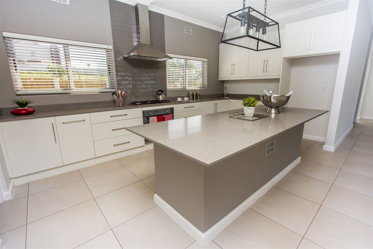 Modern kitchen featuring a central island, stone countertops, built-in oven, gas hob, stainless steel extractor fan, and ample white cabinetry.