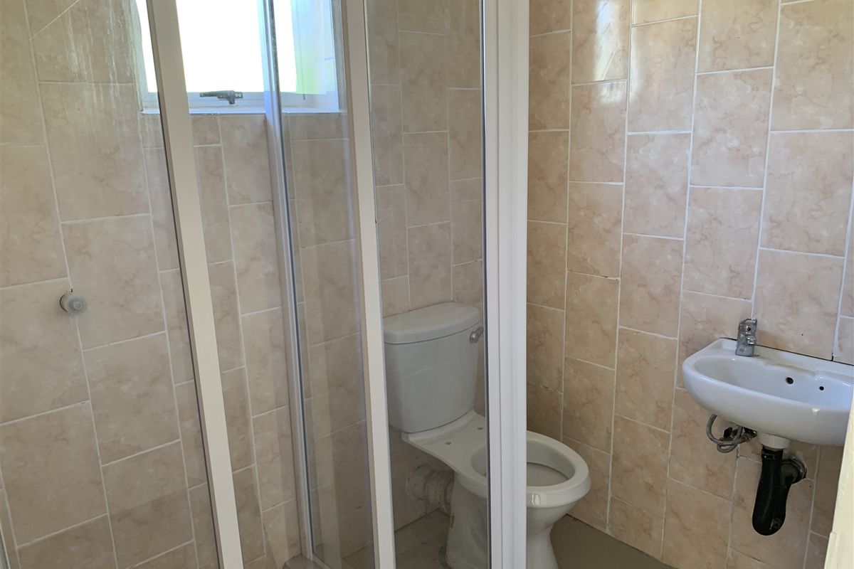 A functional bathroom featuring a shower enclosure, a standard toilet, and a wall-mounted basin with tiled walls.