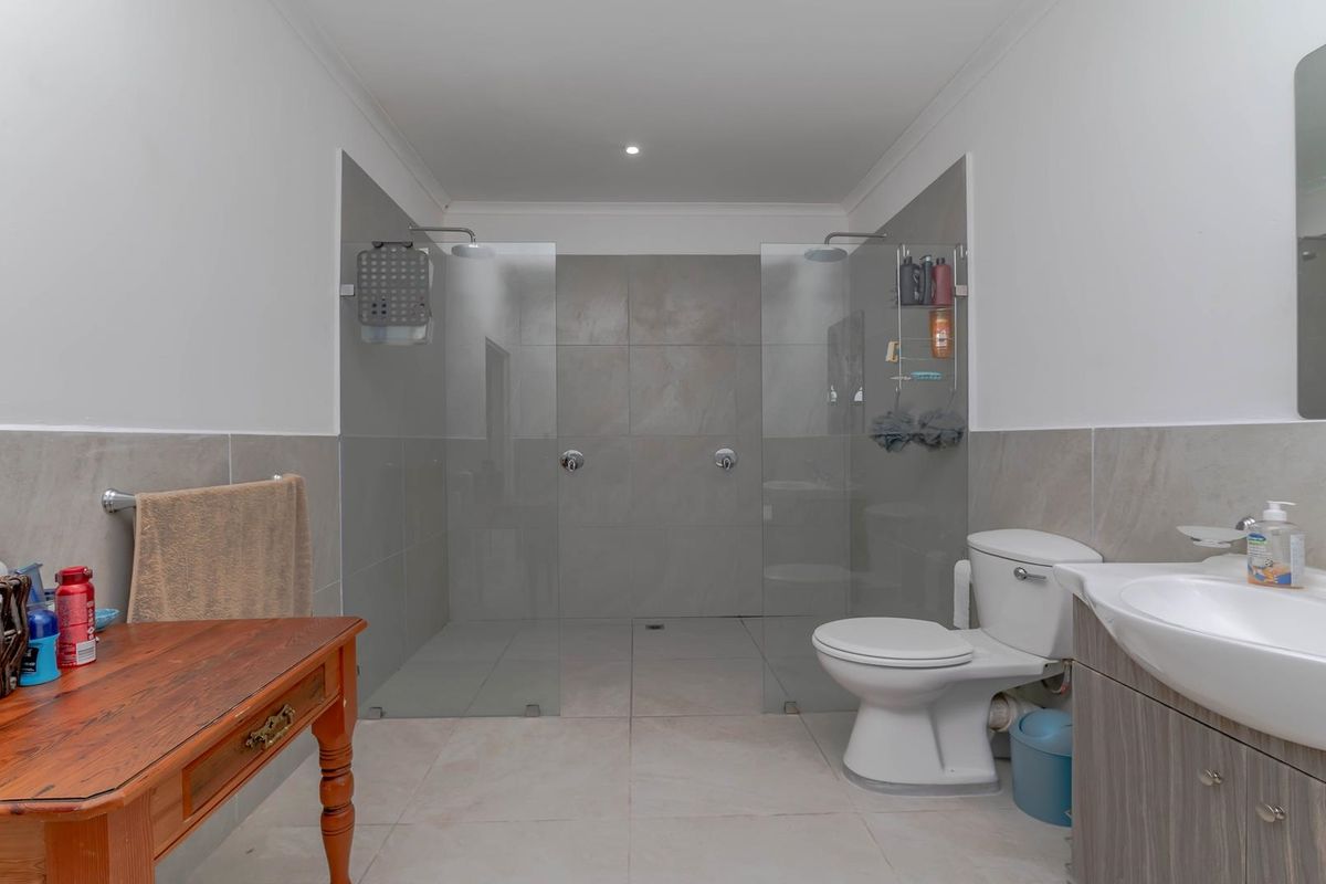 Modern bathroom featuring a spacious walk-in double shower with glass screens, a vanity unit with basin, and a toilet.