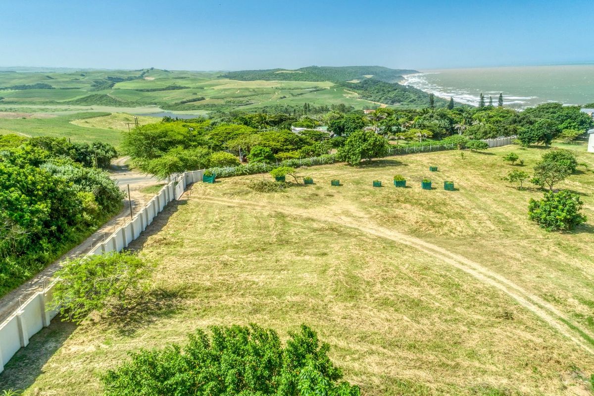 Aerial view of a vacant residential plot featuring perimeter walling, established trees, and scenic coastal landscape views.