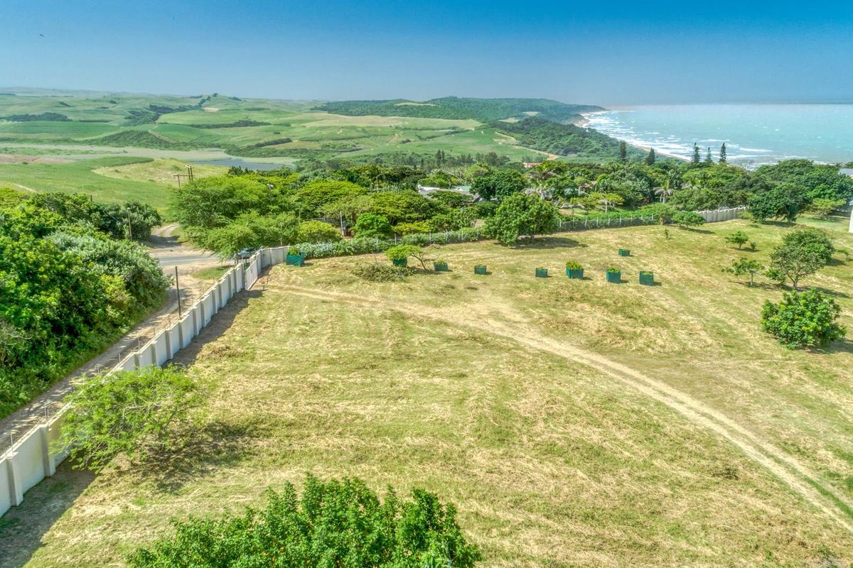 An elevated aerial view of a vacant residential plot featuring perimeter walling, established trees, and scenic coastal landscape views.