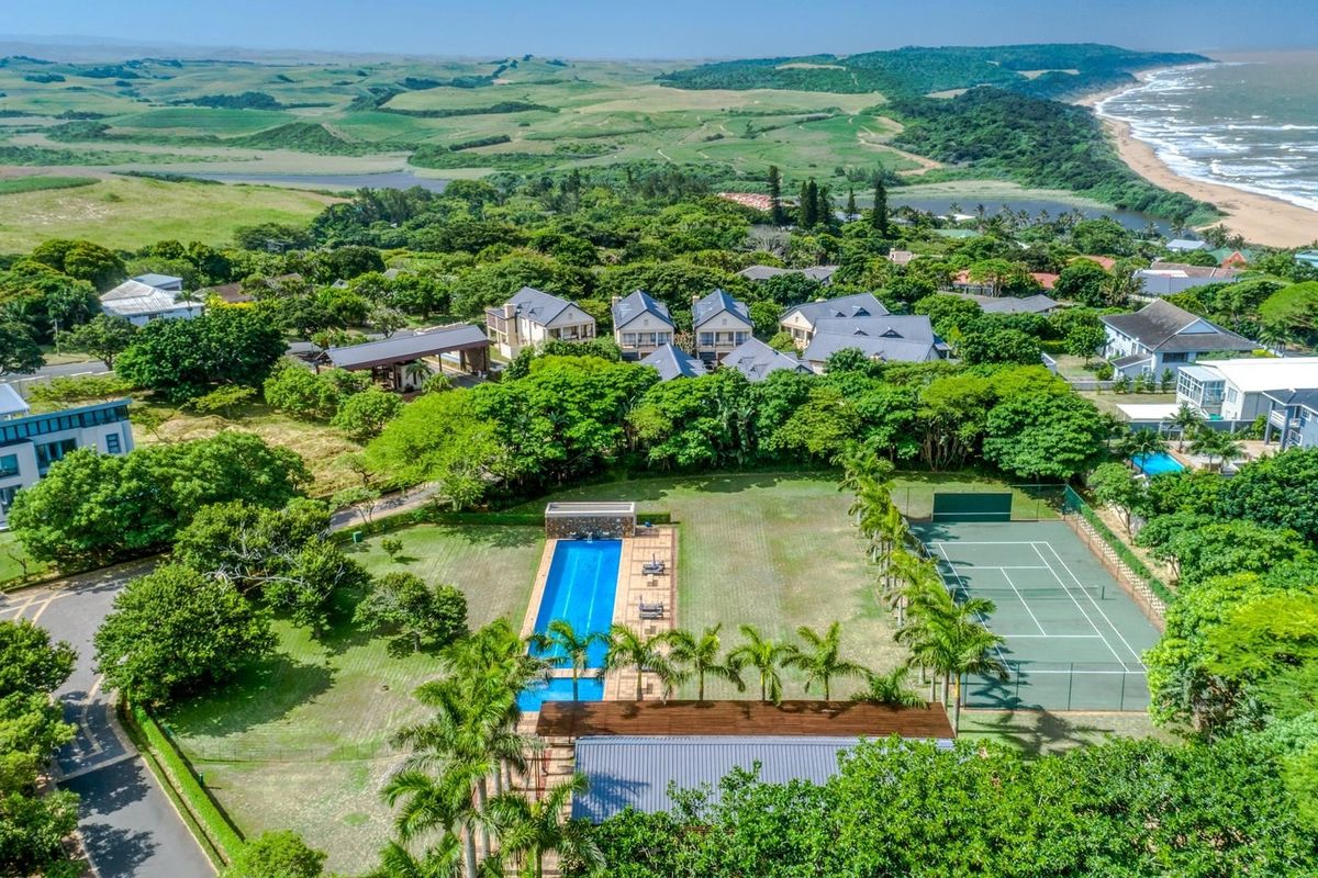 Aerial view of a residential estate featuring a swimming pool, tennis court, and lush landscaped grounds near the coastline.