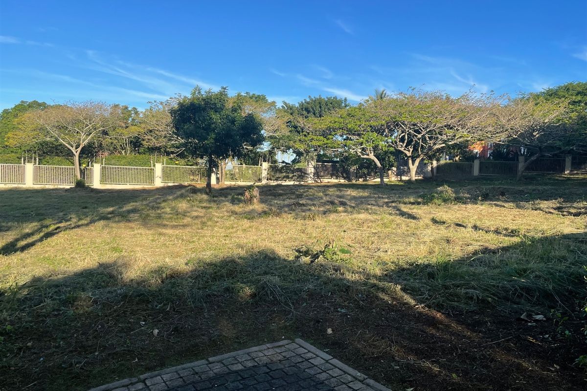 A view of a vacant residential plot featuring cleared grass, mature trees, and perimeter fencing.