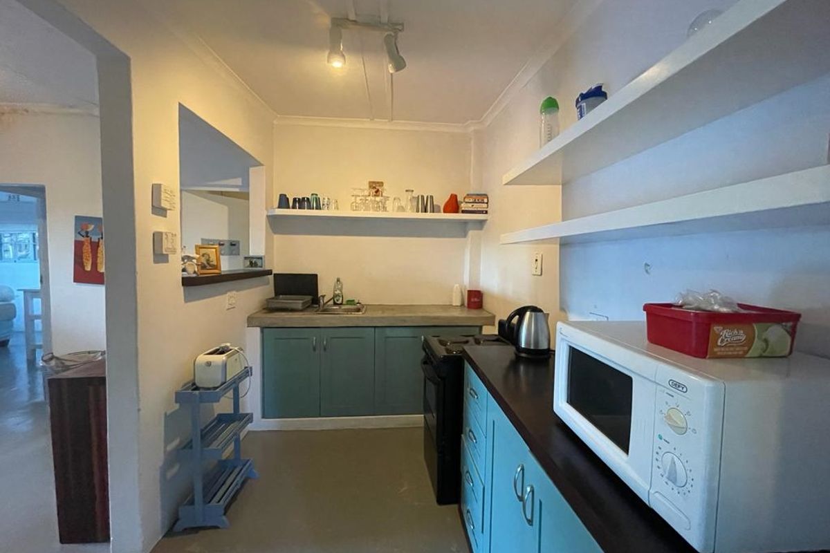 A functional kitchen featuring teal cabinetry, concrete-style countertops, open shelving, and a pass-through window connecting to the adjacent living area.