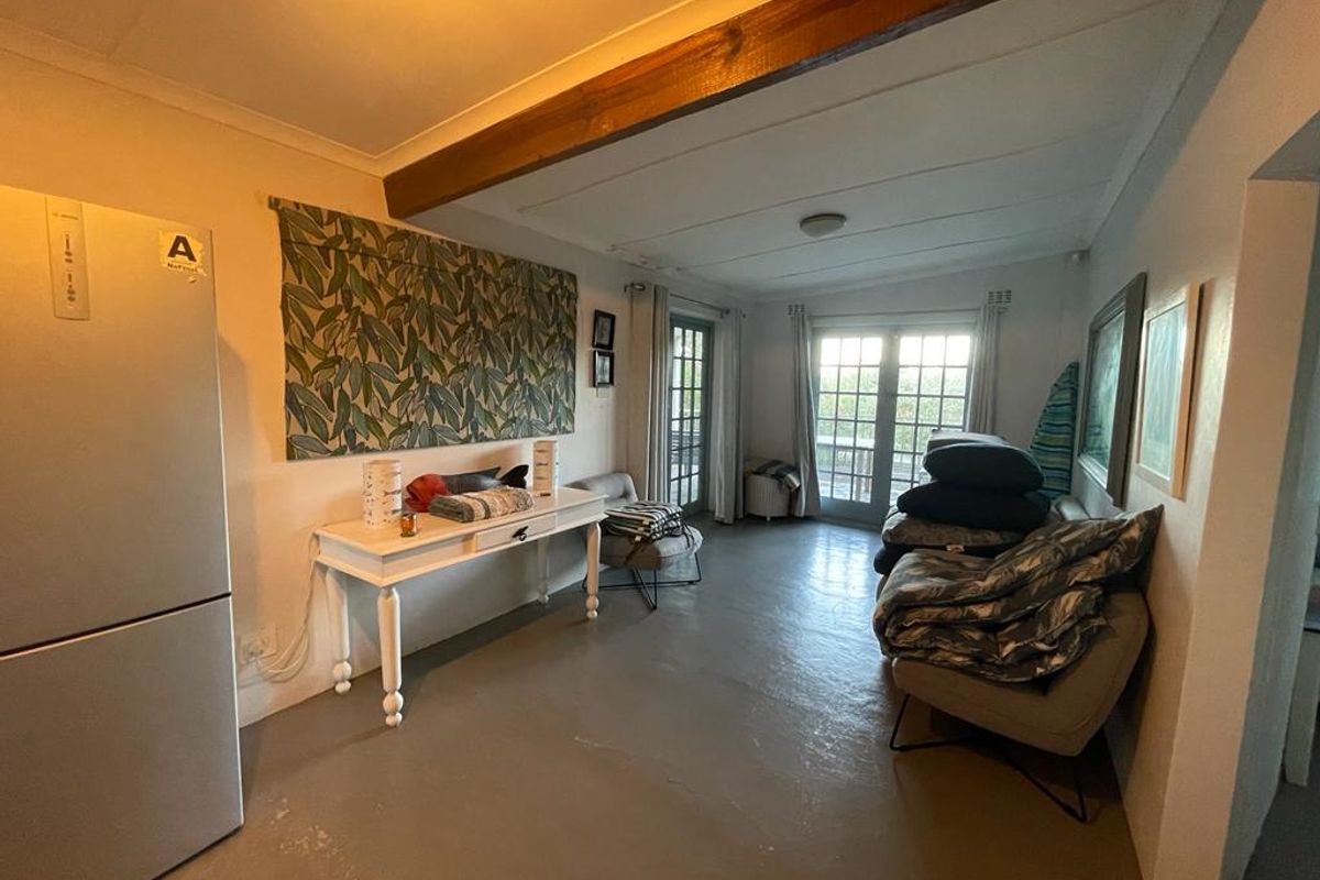 A living area featuring exposed timber ceiling beams, painted concrete flooring, and double glass doors providing access to an outdoor space.