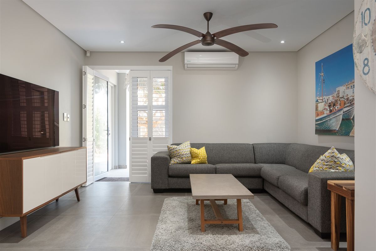 A modern living room featuring large format floor tiles, a ceiling fan, and a wall-mounted air conditioning unit, with access to an outdoor area.