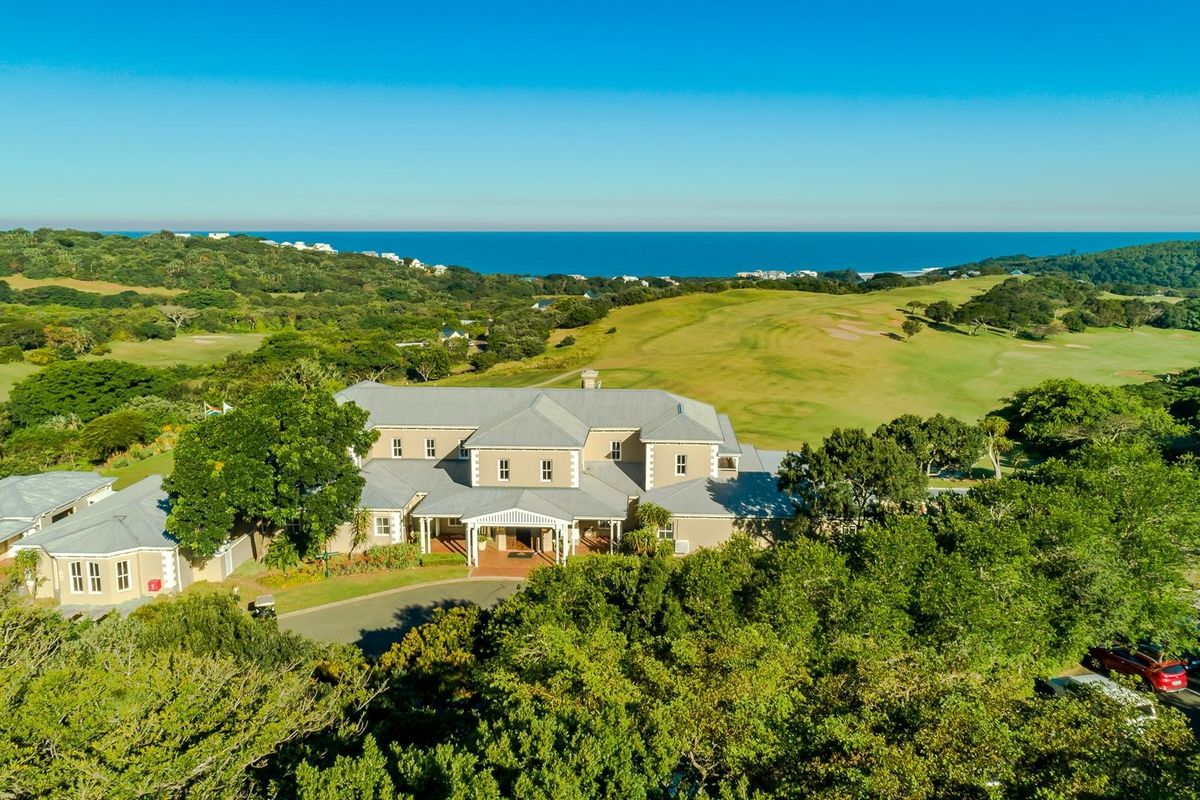 Aerial view of a large estate property featuring a multi-pitched roof design, surrounded by lush greenery and overlooking a golf course and the ocean.