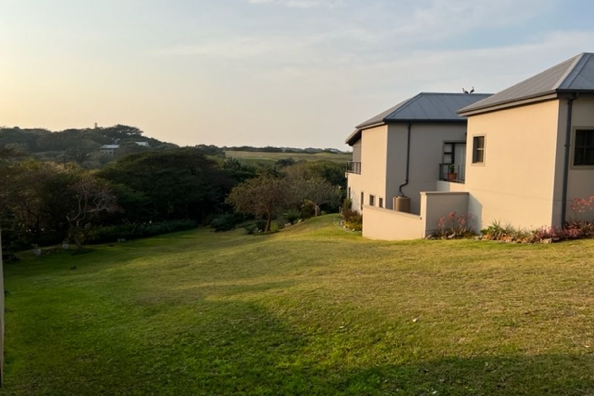 A view of the rear elevation of a residential property featuring a spacious lawn and surrounding natural landscape.