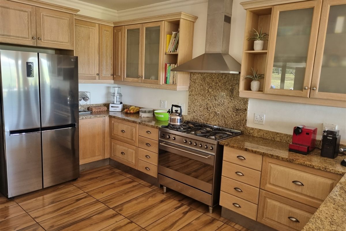 A well-appointed kitchen featuring light wood cabinetry, granite countertops, a stainless steel gas range with extractor hood, and wood-look tiled flooring.