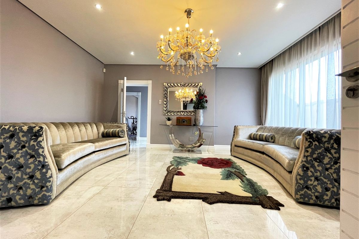 Spacious living room featuring polished marble flooring, recessed downlighting, and an elegant crystal chandelier, creating a bright and sophisticated atmosphere.