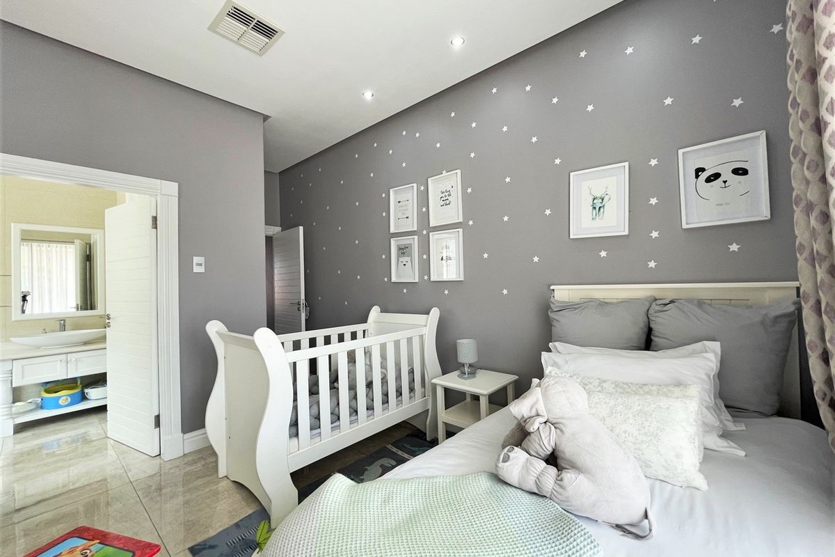 A well-maintained bedroom featuring neutral grey walls, recessed ceiling lighting, and tiled flooring, with an adjoining en-suite bathroom visible through the doorway.