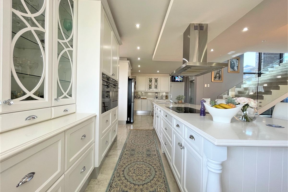 Modern open-plan kitchen featuring high-end cabinetry, a large central island with a built-in cooktop, stainless steel extractor fan, and integrated appliances.