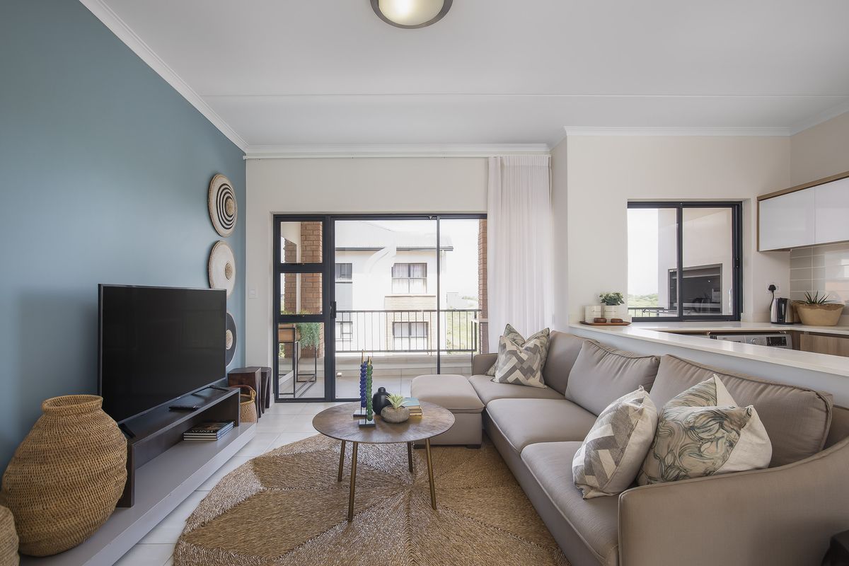 Modern open-plan living area featuring a kitchen with built-in cabinetry and a sliding door leading to a balcony, finished with neutral tones.