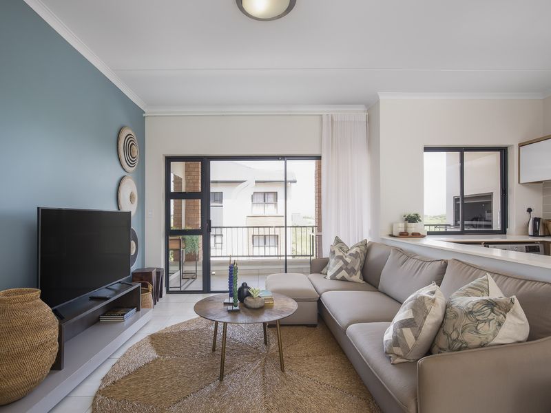 Modern open-plan living area featuring a kitchen with built-in cabinetry and a sliding door leading to a balcony, finished with neutral tones.