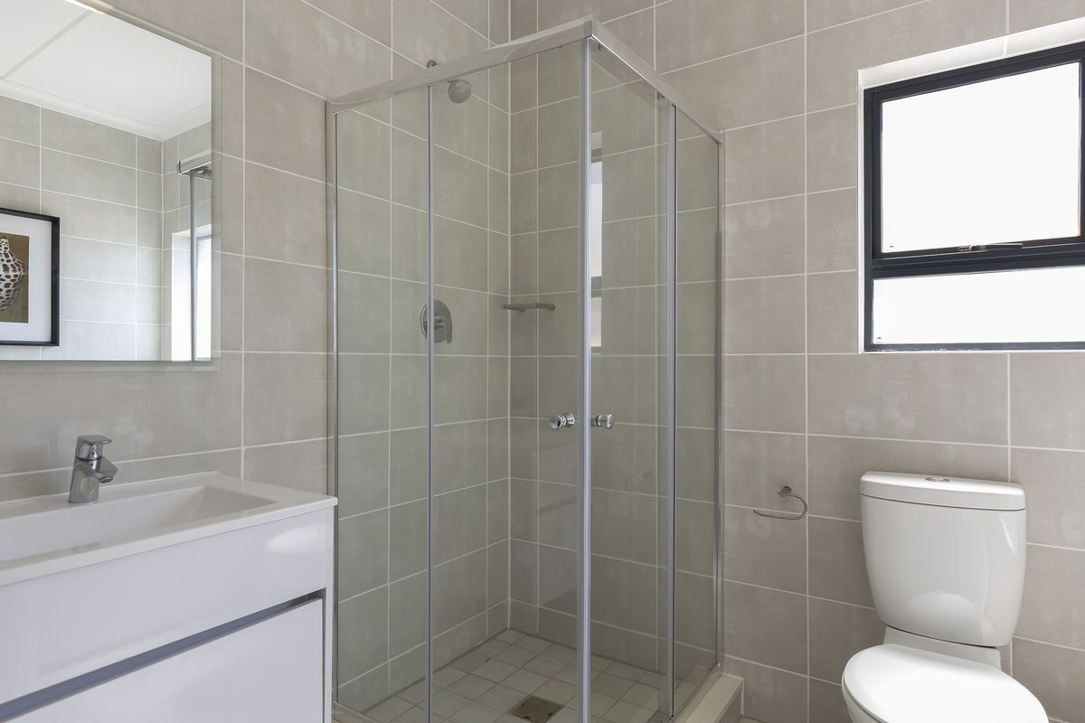 A clean, modern bathroom featuring a glass-enclosed shower, vanity basin, and neutral wall tiling.