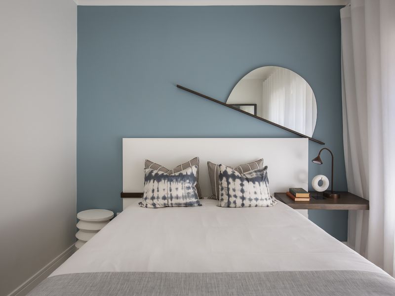 A well-maintained bedroom featuring a blue accent wall, a custom white headboard, and a floating wooden bedside shelf.