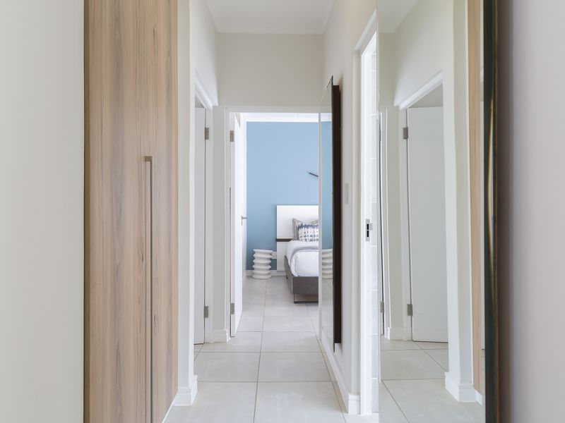 A clean, modern hallway featuring light-toned tiled flooring and integrated wood-finish cabinetry, leading towards a bedroom.