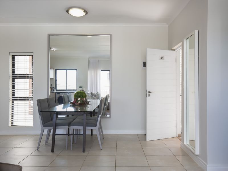 Open plan living area featuring neutral tiled flooring, a large wall-mounted mirror, and clean white finishes, creating a bright and welcoming atmosphere.