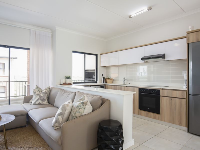 Modern open-plan kitchen and living area featuring sleek cabinetry, integrated appliances, tiled flooring, and direct access to a balcony through sliding glass doors.
