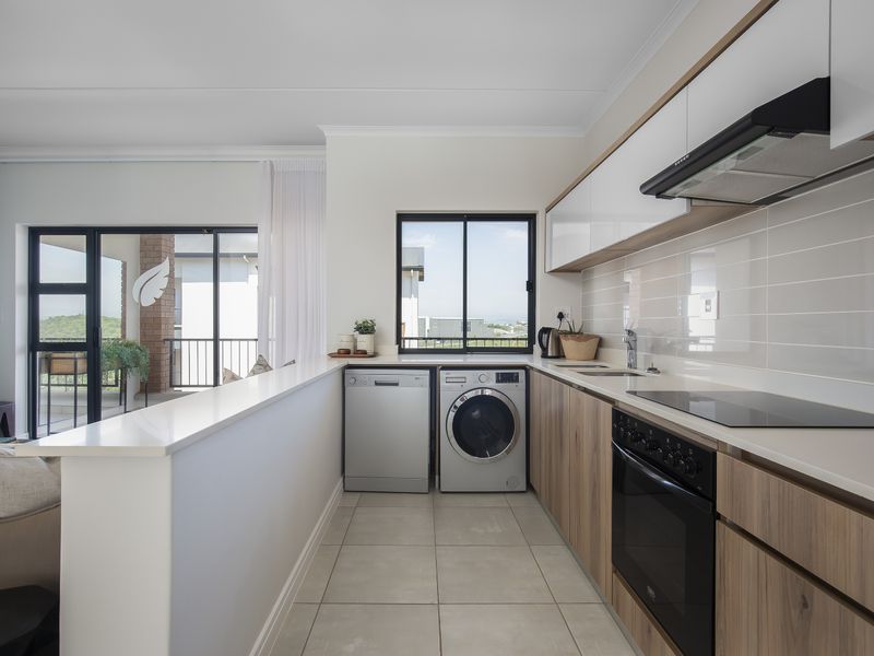 Modern open-plan kitchen featuring sleek wood-finish cabinetry, stone countertops, integrated appliances, and direct access to a private balcony.